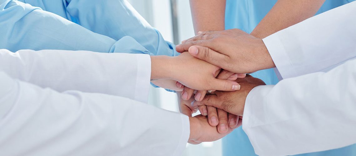 Close-up image of doctors and nurses stacking hands and expressing support