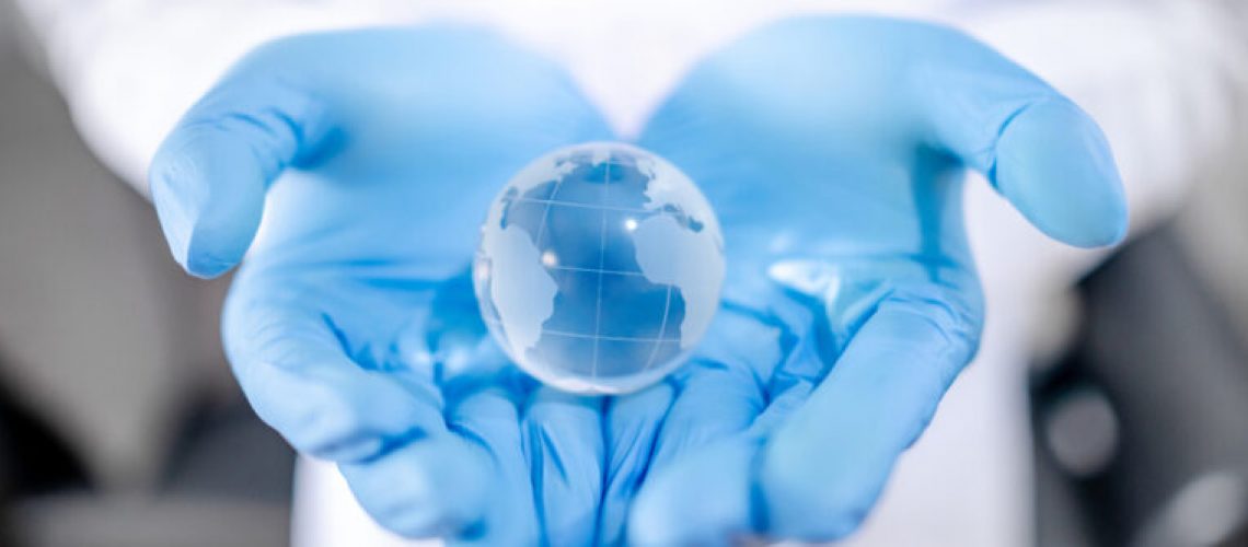 Global health and medicine. Heal the world concept. Doctor, nurse or medical worker in white protective suit with blue sterile rubber gloves holding world globe crystal glass ball in hand.